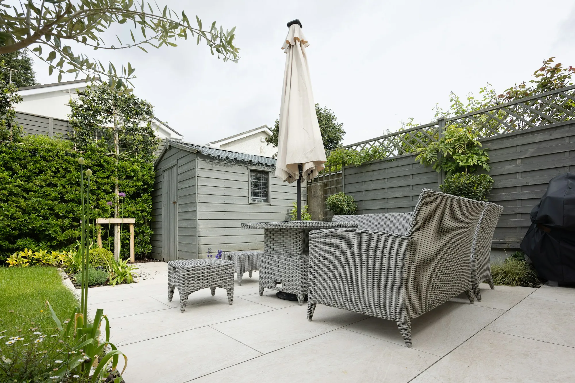 Concrete patio with wicker chairs and an umbrella in a fenced yard